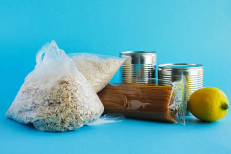 Food assistance, donations. Basic necessities, oatmeal, rice, pasta, canned food, vegetables on a blue background.の写真素材
