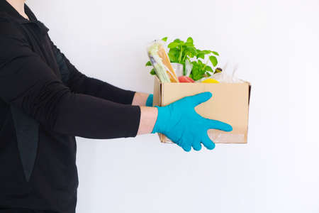 Food delivery during quarantine. Grocery basket, donation, help. Men's hands hold a cardboard box with groceries, cereals, canned food, vegetables and fruits.の写真素材