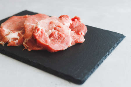 Raw fresh pork stacks do not lie on a black stone board on a gray background. Save the space. Meat preparation.の写真素材