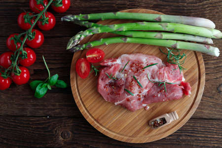 Top view on pork chops in spices on a wooden table with fresh green asparagus and cherry tomatoes. Grilled vegetables and meatの写真素材