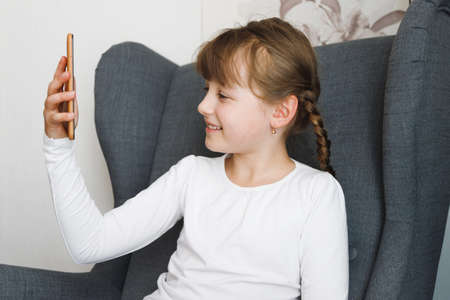 A cute seven-year-old European little girl with brown hair communicates via telephone with friends...