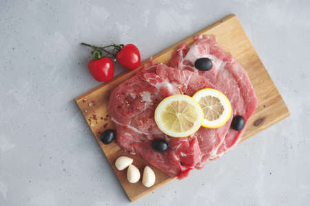 Top view on pickled pork steaks with garlic cloves, black olives and lemon on a wooden board. Preparation for grilling, frying meatの写真素材