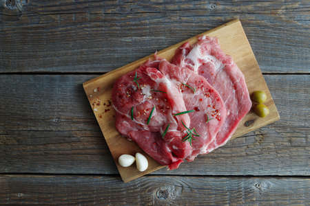 Fresh raw meat, pork steaks in spices with olives and garlic on a wooden board on an old rustic wooden table. Copy space.の写真素材