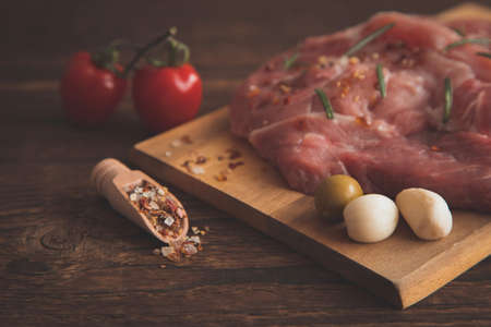 Close-up on pickled pork steaks and next to a wooden spoon, stingy, scoop with spices, all this lies on a wooden backgroundの写真素材