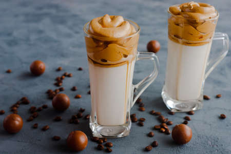 Trendy, trendy Dalgon coffee drink made from vegetable or regular milk with coffee foam. Two glasses stand on a black background and next to the candy.の写真素材
