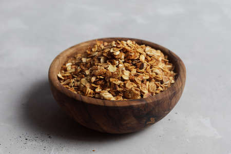 Wooden bowl, plate full of freshly cooked homemade oatmeal granola on a light gray background.の写真素材