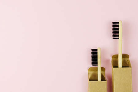 Two natural eco toothbrushes made of wood in cardboard packaging. Pink background, place for text. Oral careの写真素材
