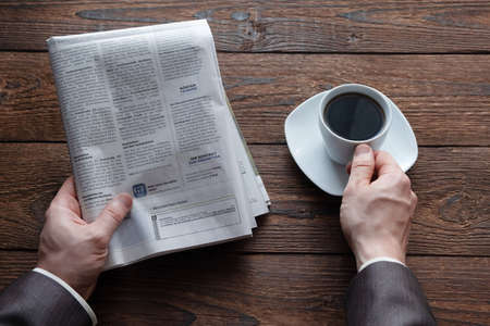 Top view on male hands holding a German newspaper and a cup of black coffee. Reading the news in the morning. Finance, business. Place for text.の写真素材