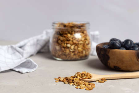 Homemade granola in a glass jar and berries in a wooden bowl nearby. In the foreground is a spoon with cereal. Healthy breakfast, the right way of life.の写真素材