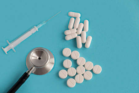 Medical stethoscope, pills, tablets and syringe on a blue background. Diagnosis of diseases and treatment. Place for text.の写真素材