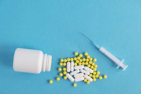 A white bottle, a jar of drugs and a handful of pills, pills, antibiotics with a syringe. Blue background. Place for text.の写真素材