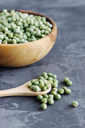 A wooden bowl full of dried green peas and a spoon nearby. Dark background, vertical orientation. Dry cereals, long-term storage products.の写真素材