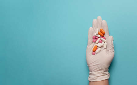 Medical banner. A gloved hand with a handful of multi-colored pills and capsules or tablets and antibiotics. Blue background. Place for textの写真素材