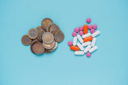 A handful of medicines, tablets or pills and next to euro coins. The price of pills, expensive pharmacology. Blue background. Place for textの写真素材
