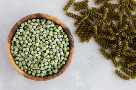 A bowl, a wooden cup with dried green peas and a row of gluten-free pasta.の写真素材