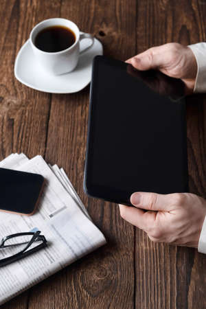 A man in a suit holds a tablet, a cup of coffee is standing nearby. Work outside the office,...