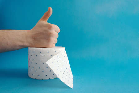 Hand with a class sign, super gesture on a toilet paper roll. Blue background. Place for text. Using...