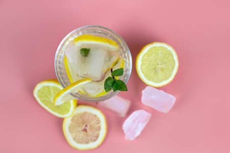 Top view on a glass of lemonade or water with lemon and pieces of ice, cocktail roll. Summer drinks, cocktails on a pink backgroundの写真素材