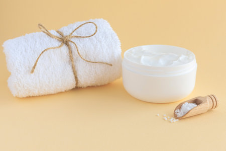 The concept of body and skin care at home. Scrub with sea salt, cream, massage brush and white terry towel on a beige background. Place for text.の写真素材
