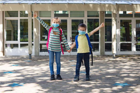 Sister and brother return to school after vacation. Children hold hands in front of school doors and...