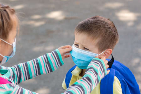 A sister helps to dress, adjusts a protective mask to her younger brother in the schoolyard. Back to...