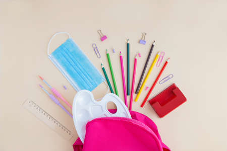 A protective medical mask and School and office supplies scattered from a pink backpack. Back to...