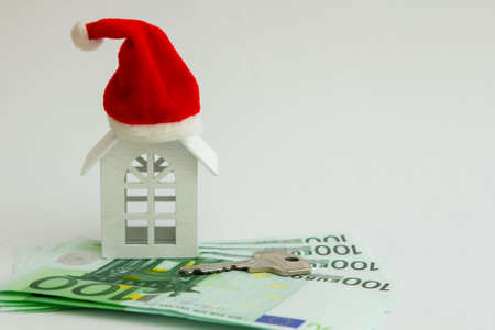 a small white house with Santa Claus hat on it stands on euro banknotes and next to it lies the key. Gift for the new year. Home purchaseの写真素材