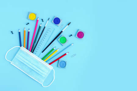 School supplies with medical protective mask on a naked background. Back to school after virus and quarantine, distance and protection while learning. Copy spaceの写真素材