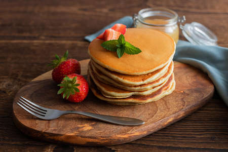 Traditional American pancakes with berries for breakfast on a wooden board over a rustic brown...