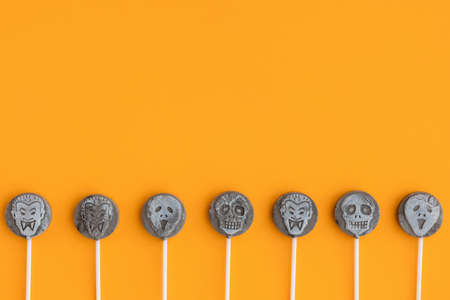 Sweets, lollipops in the form of skulls and vampires on an orange background. Spooky sweets for the holiday, Halloween. Copy space.の写真素材