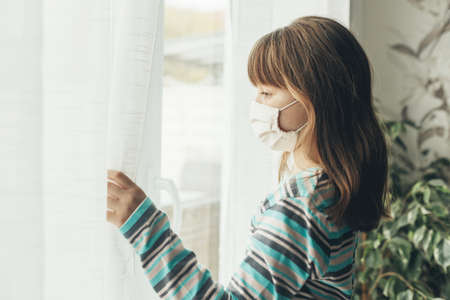 Sad Teenager Girl Mask Looks Window Coronavirus Epidemic Precaution Methods.の写真素材