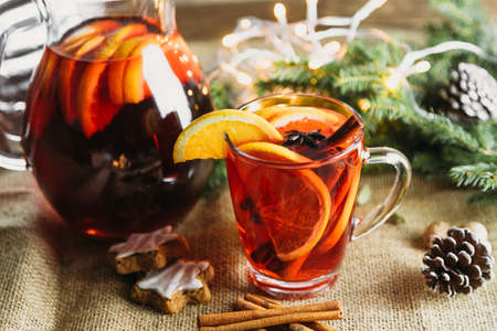 A glass of hot mulled wine with fresh orange slices and cinnamon sticks next to a decanter of wine. New Year's, winter drink.の写真素材