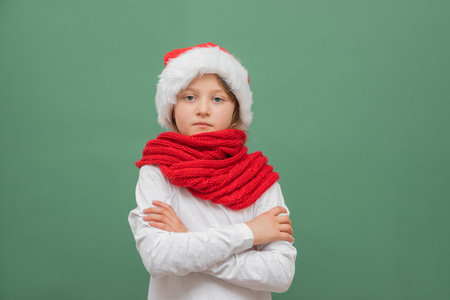 Happy new year and merry christmas. Cute little caucasian girl in a santa hat and a red scarf on a green background with place for textの写真素材