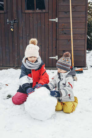 Snow time, games in the snow. Cute Caucasian children brother and sister make a snowman in the yard...