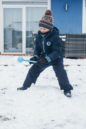 Cute caucasian boy is playing snowballs in the backyard of the house. Winter fun and games, vacations and rest.の写真素材