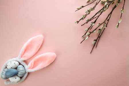 Easter, spring flat lay with colorful eggs, bunny ears and willow branches on a pastel pink...