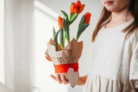 Potted tulips in the hands of a girl in a beige dress. Depersonalization. Congratulations on the holiday, mothers day or international womens dayの写真素材