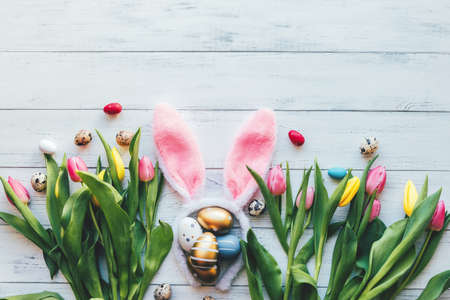 Easter layout of tulip flowers, eggs and bunny ears on a white wooden background. Spring, festive flat lay. Copy spaceの写真素材