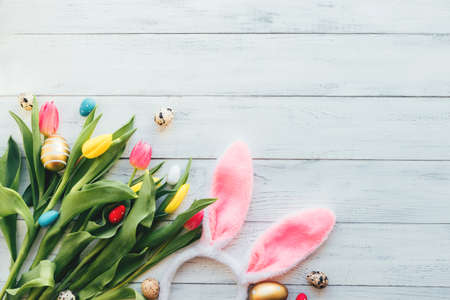Easter layout of tulip flowers, eggs and bunny ears on a white wooden background. Spring, festive flat lay. Copy spaceの写真素材
