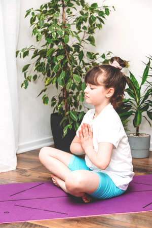 Cute caucasian girl doing gymnastics, fitness or yoga at home on a pink mat. Sports, stretching for children, online lessons and training.の写真素材
