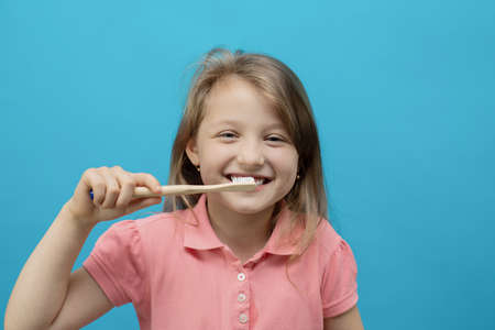 Dental concept. Close-up portrait of a pretty girl who brushes her teeth with an ecological brush on a blue background. Oral care, caries prevention.の写真素材