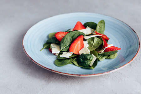 Fresh salad of fresh spinach leaves, strawberries and blue cheese, seasoned with raspberry vinegar on a blue plate. Vegetarian, raw food.の写真素材
