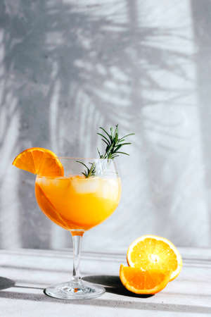 Refreshing cocktail with an orange and a sprig of rosemary in the rays of the bright sun with a shadow from a palm branch. Chilled summer drinks.の写真素材