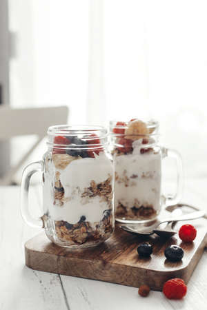 A healthy, dietary breakfast or snack of granola or oatmeal muesli with yoghurt and fresh wild berries. Ideal for vegetarians. Light background and vertical photo.の写真素材