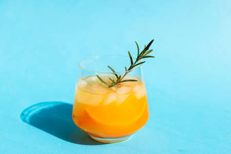 Refreshing cocktail with orange and rosemary sprig on a blue background. Summer drinks. Copy spaceの写真素材