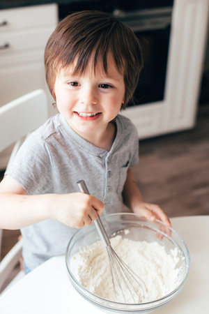 Adorable cheerful boy, Toddler kneads dough in the kitchen. Children cat dough at home.の写真素材