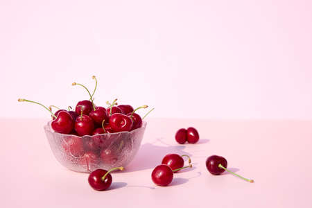 Glass bowl full of fresh and juicy cherries on a pink and white background. Place for your text....
