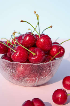 Close-up of fresh, juicy, organic cherries in a glass bowl against a pink pastel background....