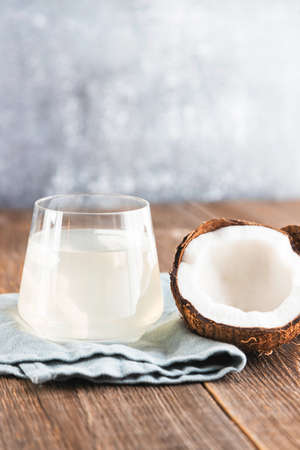 A glass of fresh, organic coconut water, milk on a wooden table and half a juicy coconut next to it....
