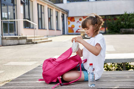 A schoolgirl gets out of her backpack her lunch, a sandwich in the schoolyard. Children eat at school, school snacksの写真素材